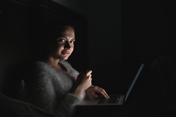 cute young girl sitting in bed late at night in the dark, watching a scary movie on laptop - Fotografie, Obrázek