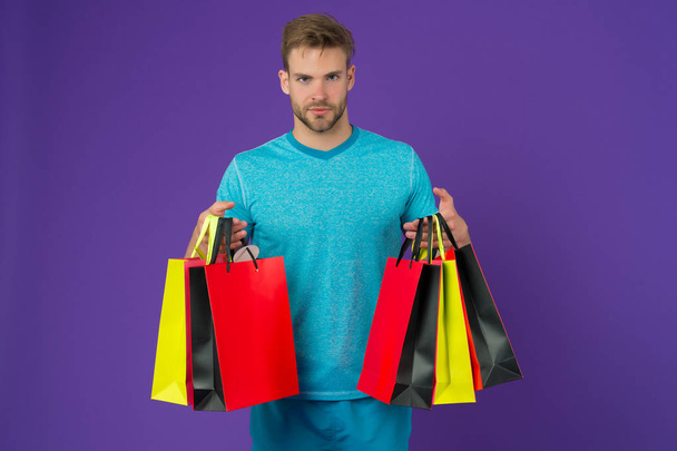 Man with shopping bags on violet background. Macho with colorful paper bags. Fashion shopper in casual blue tshirt. Holidays preparation and celebration. Shopping or sale and cyber monday. - Foto, Imagem