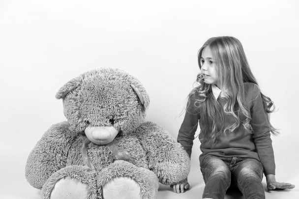 Girl sit with big teddy bear on orange background. Child with grey soft toy. Holiday, birthday, anniversary celebration. Kid with animal doll, present and gift. Happy childhood concept. - Фото, изображение
