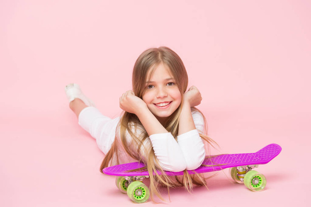 Small girl smile with skate board on pink background. Child skater smiling with longboard. Skateboard kid lie on floor. Childhood lifestyle and active games. Sport activity and energy, punchy pastel. - Photo, image