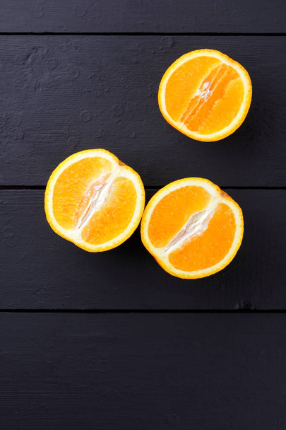 Fruits of oranges on a black wooden background, halves of oranges on wooden boards. Copy space. Citrus for Vegetarian Breakfast - Fotografie, Obrázek