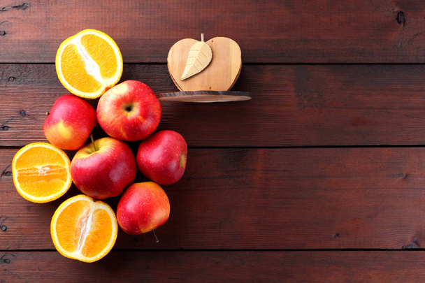 Fruits of oranges and red apples on a dark brown wooden background, halves of oranges on wooden boards. Copy space. Citrus fruits and apples for vegetarian breakfast - Photo, Image