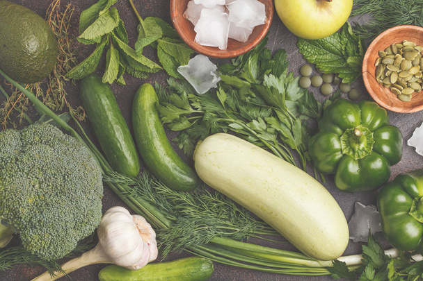 Green vegetables on a dark background. Vegetable vegan diet food background: zucchini, peppers, broccoli, cucumbers, avocado, apple, herbs. Healthy lifestyle concept. - Fotografie, Obrázek