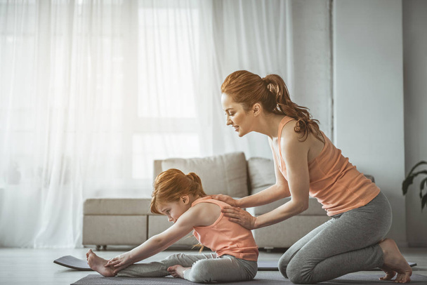 Red-haired mother and kid training in living room - 写真・画像