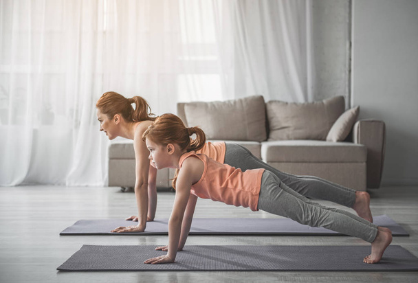 Woman and her daughter doing plank exercise at home  - Foto, immagini