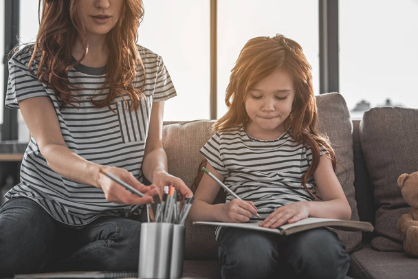 Cute focused kid drawing something with her mom at home - Foto, Bild