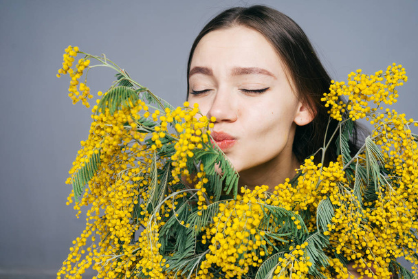 lovely young girl sniffs a fragrant yellow mimosa, enjoys the spring - Fotoğraf, Görsel