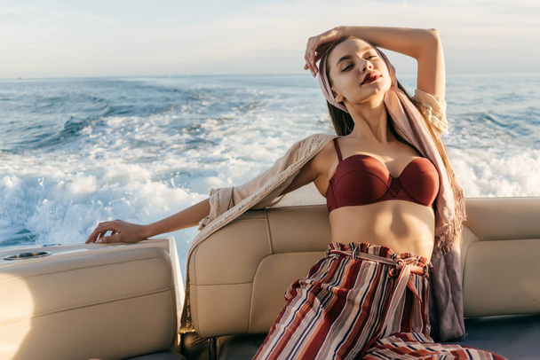 a luxurious young girl in stylish clothes enjoys a sea voyage on a yacht, posing in the rays of the sun - Foto, afbeelding
