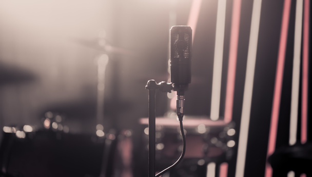 Microphone in recording Studio or concert hall close-up, with drum set on background out of focus. Beautiful blurred background of colored lanterns. Musical concept in vintage style. - Photo, Image