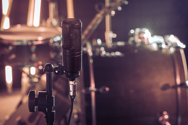 The microphone in a recording Studio or a concert hall close up of drum kit and an acoustic guitar in the background. Beautiful blurred background of colored lanterns. Musical concept in vintage style - Photo, Image