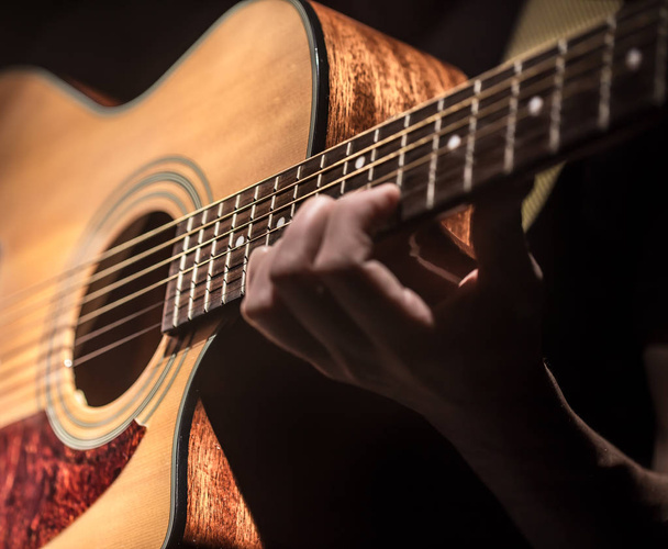 Man akoestische gitaar spelen op donkere achtergrond, gitaar close-up. Een muzikaal concept. - Foto, afbeelding