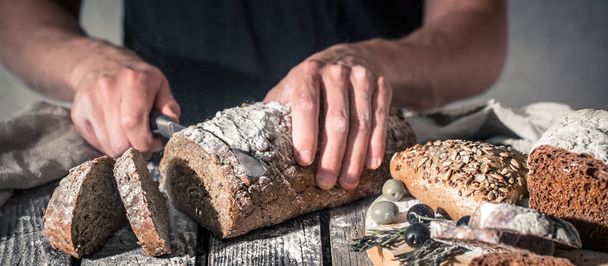 il panettiere taglia il pane fresco su uno sfondo di legno bello, il concetto di cibo sano e industria di panetteria
 - Foto, immagini