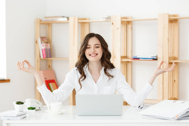 Concepto de negocios y salud: Retrato de mujer joven cerca de la laptop, practicando meditación en el escritorio de la oficina, frente a la computadora portátil, clases de yoga en línea, tomando un descanso por un minuto
. - Foto, Imagen