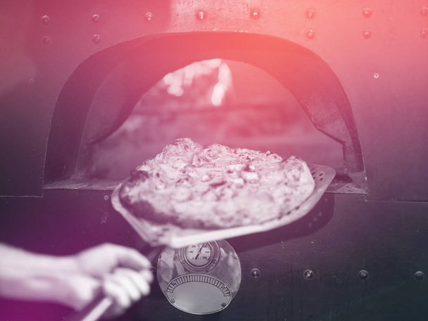 chef using special shovel to removing hot pizza from  stove where it was baked - Foto, imagen