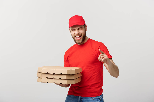 Koncepcja dostawy: Przystojny dostawca pizzy kurier w czerwonym mundurze z czapką trzymającą pudełka po pizzy. Odizolowane na biało. - Zdjęcie, obraz