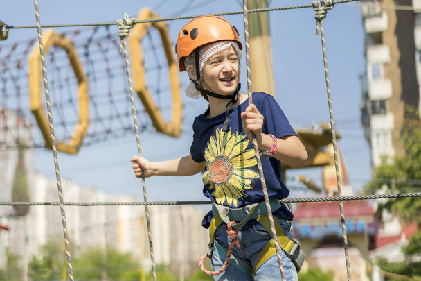cute baby girl in climbing gear on a rope park background. Little beautiful girl climbs on rope harness in summer city park - Foto, Imagen