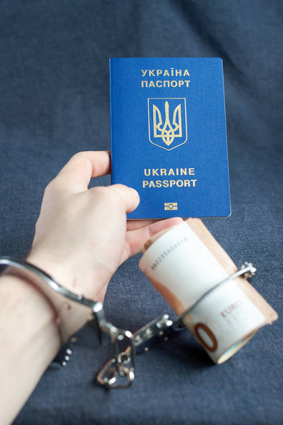ukrainischer biometrischer Pass und Handschellen am Arm mit Geld auf dem Tisch - Foto, Bild