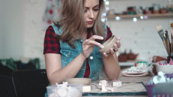 若い女性は、ワーク ショップで粘土の板を作成します。少女は、彼女の手で粘土の形を保持しています。創造的な趣味 - 映像、動画