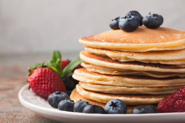 Close-up delicious pancakes, with fresh blueberries, strawberries and maple syrup on a rusty background. With copy space. - Foto, Imagen