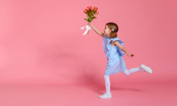 αστείο παιδί κορίτσι τρέχει και πηδάει με μπουκέτο από λουλούδια σε ένα χρωματιστό backgroun - Φωτογραφία, εικόνα