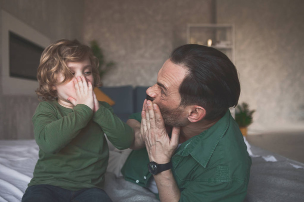 Уходящий сын гримасничает с радостным отцом
 - Фото, изображение