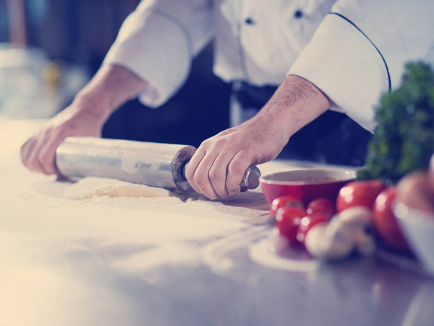 chef preparing dough for pizza rolling with rolling pin on sprinkled with flour table - Photo, Image