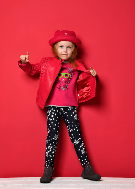 Five years old baby girl child kid posing in red leather jacket and hat pointing finger up on red - Фото, зображення
