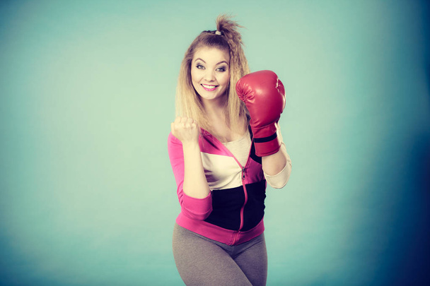 Funny blonde girl female boxer in big fun red gloves playing sports boxing studio shot on blue - Foto, afbeelding