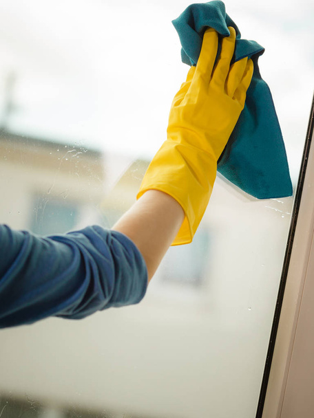 Female hand in yellow gloves cleaning window with blue rag and spray detergent. Spring cleanup, housework concept - Photo, image
