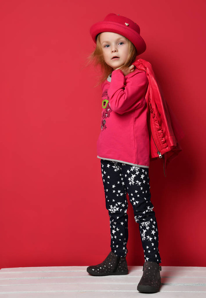 Five years old baby girl child kid posing in red leather jacket and hat  on red - Fotó, kép