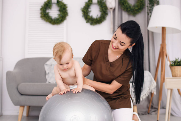Une masseuse professionnelle avec bébé heureux faisant des exercices avec balle de remise en forme à la salle médicale. Soins de santé et concept médical
. - Photo, image