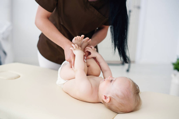 Gesundheitsfürsorge und medizinisches Konzept. eine professionelle weibliche Masseurin macht eine Massage und Gymnastik für ein kleines Baby in einem modernen gemütlichen Raum. - Foto, Bild
