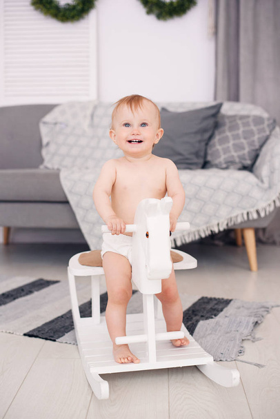 Smiling little baby playing on a wooden toy horse in cozy room. - Valokuva, kuva