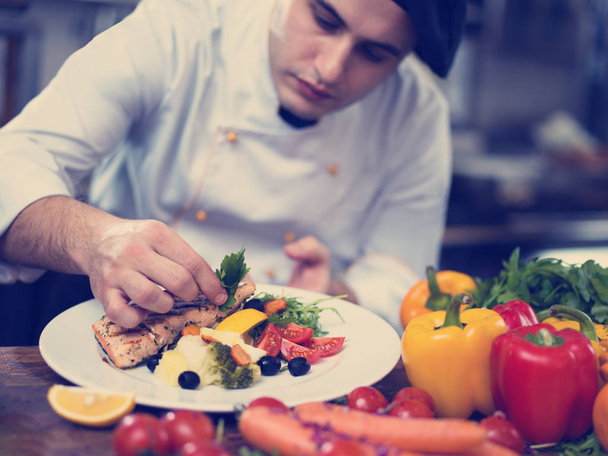 cook chef decorating garnishing prepared meal dish on the plate in restaurant commercial kitchen - Photo, image