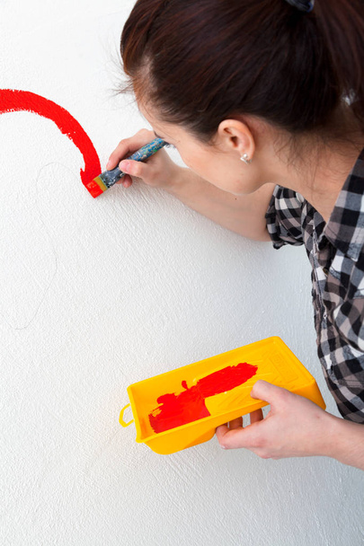 Close-up of a woman artist paints on a wall with a large wooden tassel in red - Foto, Imagem
