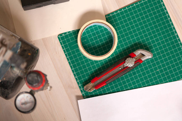 Un primer plano de un conjunto de herramientas: un cuchillo de corte de papel, un papel milimétrico, una cinta adhesiva, un airgrove. Vista desde arriba
 - Foto, imagen