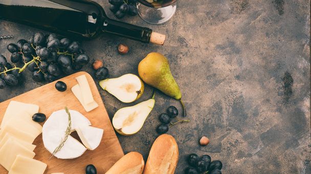 Cheese platter with a grapes. Camembert or brie cheese on wooden board. Baguette, bottle of red wine, pears on metal background. Copy space - 写真・画像