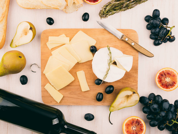 Vegyes sajttál a szőlő. Camembert és brie sajtot a deszkán. Baguette, üveg vörös bor, körte, narancs, fából készült háttér.  - Fotó, kép