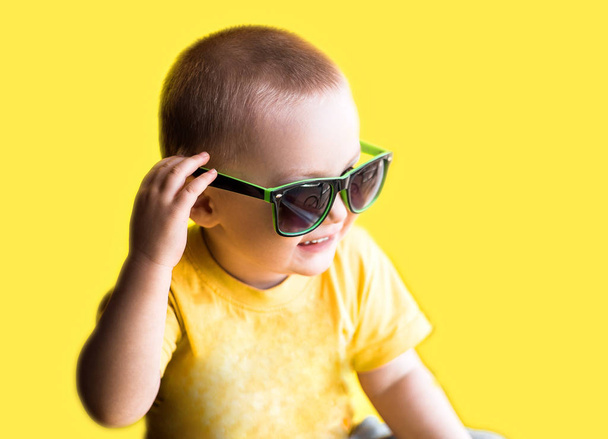 Ευτυχισμένος χαμογελαστό αγόρι στο κίτρινο t-shirt και πράσινα γυαλιά ηλίου, παιδική ηλικία, μόδα και άνθρωποι έννοια, σε κίτρινο φόντο, θερινή ώρα - Φωτογραφία, εικόνα