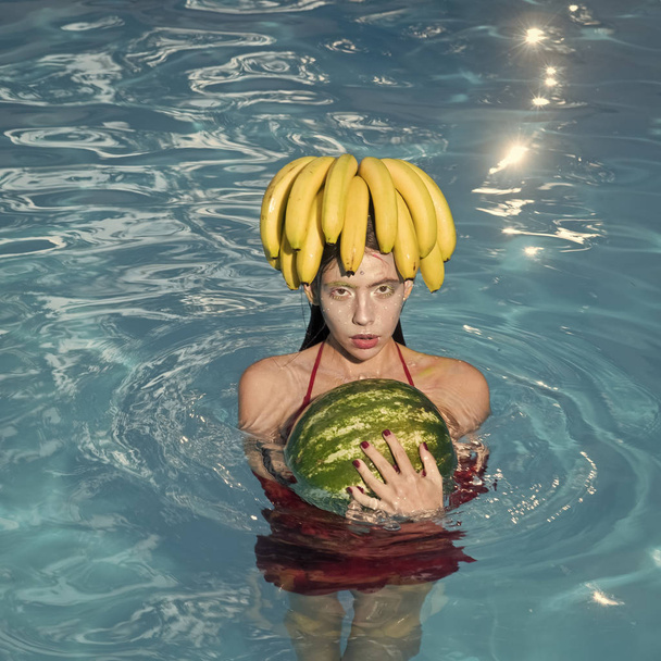 Fashion woman model posing. Girl on beach hold watermelon and banana in the blue pool. Tropical fruit diet. Summer holiday idyllic. - Foto, Imagen