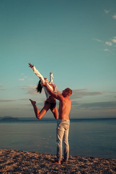 Nude couple and erotic moments. Couple in love dancing, having fun, sea and skyline background. Couple in love stand on beach, seashore. Honeymoon, just married concept. Man carries woman - Zdjęcie, obraz