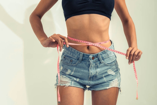 Jonge slanke vrouw meet haar taille door meetlint na dieet tegen een witte achtergrond. Concept van succes van het verlies gewicht. - Foto, afbeelding