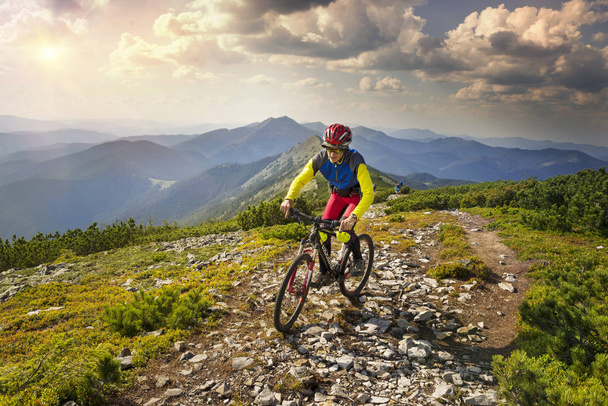 Racer on the Alpine stone path in the Carpathians with a carbon mountain bike of the sports group as a symbol of the health of the modern lifestyle of a young progressive person - Photo, Image
