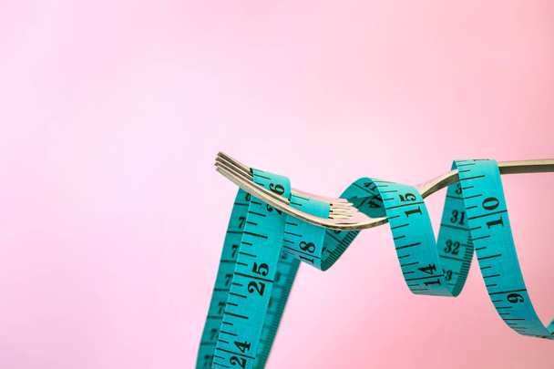 Диета для похудения, измерительная лента с вилкой на светло-розовом фоне для заботы о здоровом питании
 - Фото, изображение