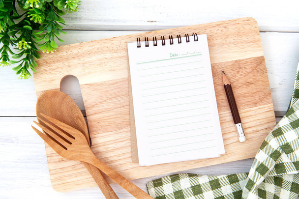  lined book notepad paper on chopping cutting board and tablecloth with wooden fork and spoon on white table , recipes food  for healthy habits shot note background concept - 写真・画像