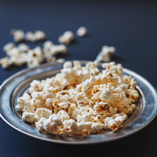 Tasty source of dietary fiber. Popcorn in a metallic plate on a dark painted matte surface. Shallow depth of field. - Фото, изображение