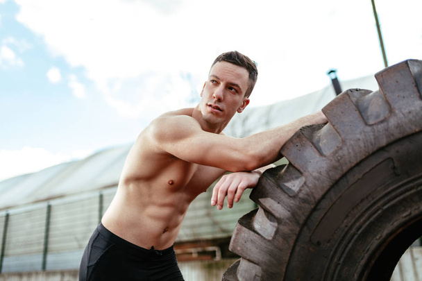 Молодий м'язистий чоловік піднімає величезні шини для тренування м'язів на стадіоні
 - Фото, зображення
