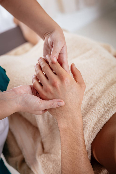 Weergave van de hads van jonge vrouwelijke therapeut masseren man hand bij schoonheidssalon sluit - Foto, afbeelding
