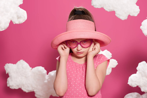 μόδας κορίτσι θέτοντας σε ροζ φόντο με σύννεφα, ροζ φόρεμα και καπέλο - Φωτογραφία, εικόνα
