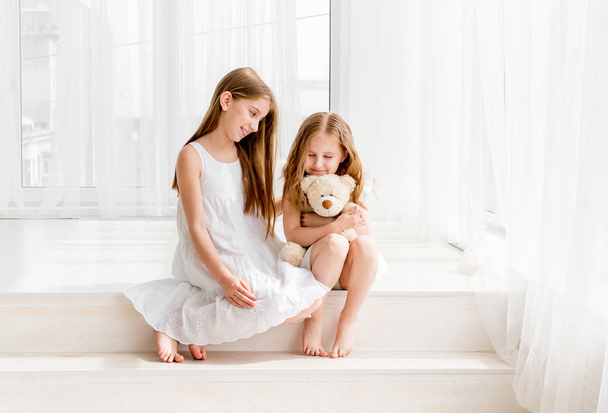 Little girl giving her teddy bear toy to older sister - Fotografie, Obrázek